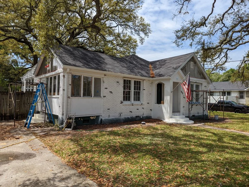 Light-colored house beneath trees with ladders at the front